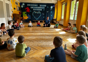 Przedszkolaki siedzą w dużym kole na sali gimnastycznej.