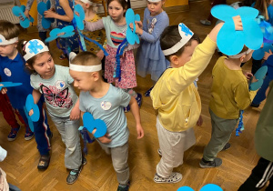 Przedszkolaki tańczą z niebieskimi motylami w ręku.
