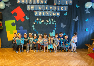 Maluchy pozują do zdjęcia pod dekoracją z Dnia Świadomości Autyzmu.
