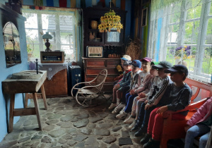 Dzieci siedzą we wnętrzu chaty gościnnej.