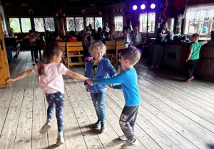 Dziewczynka i dwóch chłopców tańczą w kółeczku.