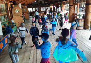Przedszkolaki poruszają się w rytm muzyki na sali tanecznej.