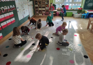 Dzieci siedzą na dywanie. Z rozsypanki literowej układają wyrazy.