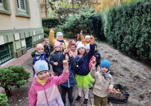 Średniaki stoją z podniesionymi do góry dłońmi, w których trzymają sadzonki.