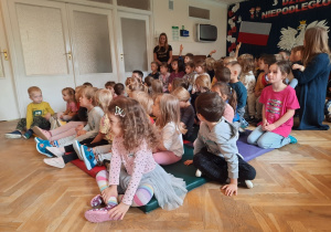 Dzieci siedzą na materacach i ławeczkach, grzecznie czekają na występ.