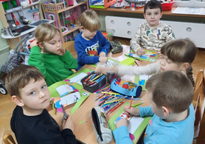 Dwie dziewczynki i czterech chłopców siedzą przy stoliku i pracują nad książeczką o prawach dziecka.