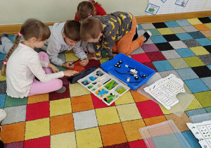 Chłopiec trzyma w ręku klocki, a dziewczynka wskazuje mu instrukcję na tablecie.