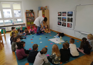 Dzieci siedzą w półkolu, a prowadząca warsztaty Labolo chodzi od dziecka do dziecka i daje im powąchać preparat znajdujący się w probówce.