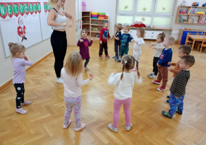 Przedszkolaki stojąc w kole prezentują za pomocą gestów grę na instrumentach podanych w piosence.