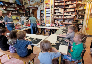 Dzieci siedzą przy stolikach ustawionych w kole w Pracowni Ceramicznej Amfora i lepią figurki z gliny.