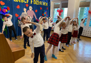 Dzieci stoją w trzech rzędach, każda para w tańcu tworzy z rąk serduszka poprzez połączenie ze sobą rąk.