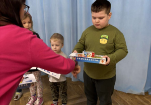 Nauczycielka wręcza chłopcu dyplom i nagrody za udział w konkursie fotograficznym.