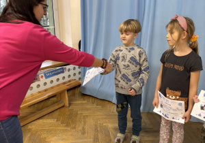 Nauczycielka wręcza chłopcu dyplom i nagrody za udział w konkursie fotograficznym.