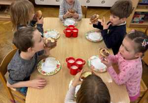 Trzech chłopców i trzy dziewczynki siedzą przy stoliku i zajadają się pysznymi pączkami.