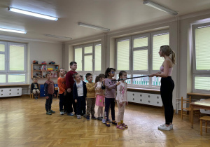 Dzieci stoją ustawione w pociąg na sali i słuchają jak prowadząca zumbę tłumaczy im kolejną zabawę.