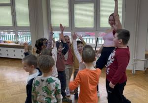 Dzieci stoją ustawione koło prowadzącej z rękami w górze i żegnają się po zakończonych zajęciach z zumby.