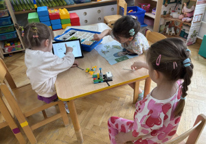 Trzy dziewczynki siedzą przy stoliku i budują konstrukcję z klocków Lego na warsztatach z robotyki.