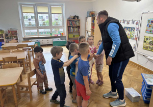 Dzieci stoją w kole, trzymając jedną rękę na ręku prowadzącego i przygotowują się do pożegnalnego okrzyku.