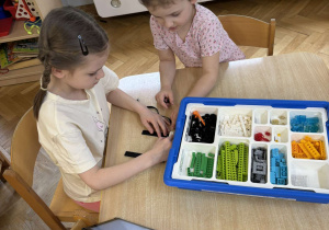 Dwie dziewczynki siedzą przy stoliku i budują konstrukcję z klocków Lego na warsztatach z robotyki.