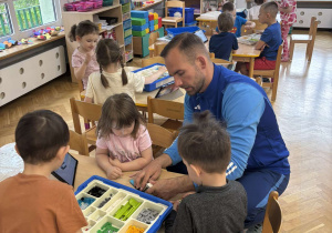 Dzieci siedzą przy stoliku i z pomocą prowadzącego budują pojazd z klocków Lego na warsztatach z robotyki.