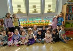 Dzieci pozują do grupowego zdjęcia z ustawionymi na parapecie doniczkami w kształcie jajek z posadzonym przez nie owsem i dekoracjami wielkanocnymi.