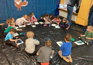Dzieci siedzą w kole na folii i malują farbami pejzaż.