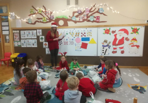 Dzieci siedzą na dywanie i słuchają pani nauczyciel, która czyta list od Świętego Mikołaja.