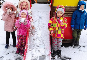 Dzieci stoją ze śnieżkami obok zjeżdżalni podczas pobytu na placu zabaw.
