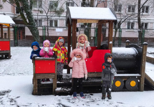 Dzieci stoją przy "pociągu" ze śnieżkami podczas pobytu na przedszkolnym placu zabaw.