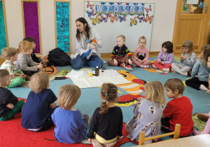 Dzieci siedzą na dywanie w półkolu i żegnają się z kukiełką Profesorka Labolka i prowadzącą.
