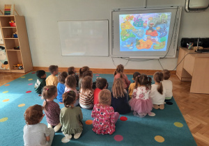 Maluchy siedzą na dywanie, na tablicy interaktywnej oglądają animację z piosenką projektową.