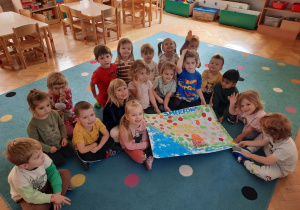 Dzieci siedzą na dywanie trzymając przed sobą grupową pracę plastyczną pt. "Smerfowa Wyspa Radości".