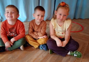 Dwóch chłopców i dziewczynka siedzą obok siebie w ubrankach i ozdobach w kolorach jesieni.