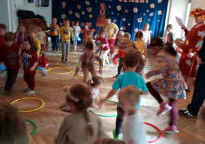 Dzieci naśladują wiewiórki, które skaczą wokół dziupli (rozłożonych na podłodze kół hula-hop).