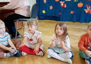 Dwie dziewczynki i dwóch chłopców śpiewają jesienną piosenkę do akompaniamentu wygrywanego na pianinie.