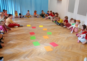 Dzieci siedzą w dużym kole, na środku rozłożone są karty A4 do jesiennej gry w memory.