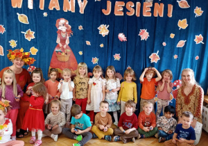 Maluchy pozują na tle dekoracji jesiennej wraz z nauczycielką grupy oraz Panią Jesienią.