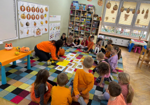 Dzieci siedzą na dywanie w półkolu, a nauczycielka zapisuje na kartce ich skojarzenia z dynią.