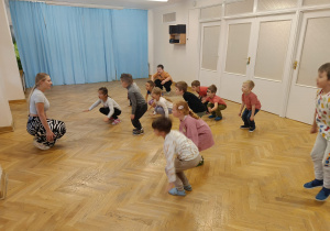 Dzieci kucają na podłodze z prowadzącą warsztaty z zumby.