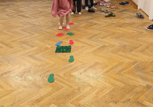 Dzieci stoją ustawione w pociąg, a dziewczynka pokonuje tor przeszkód na sali gimnastycznej.