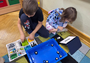 Chłopiec i dziewczynka siedzą na dywanie i budują z klocków Lego na zajęciach z robotyki.