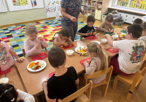 Dzieci siedzą przy stolikach i wykonują samodzielnie szaszłyki z warzyw podczas Dnia Owoców i Warzyw.