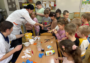 Mama chłopca przykleja dzieciom plasterki na wcześniej narysowane czerwone kreski na rękach imitujące zadrapanie w ramach projektu Bohater Tygodnia.