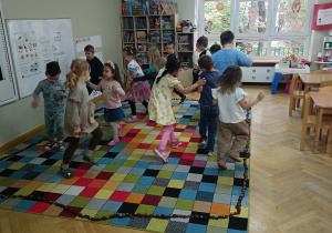 Dzieci biegają po dywanie, na którym ułożone jest koło z kasztanów.