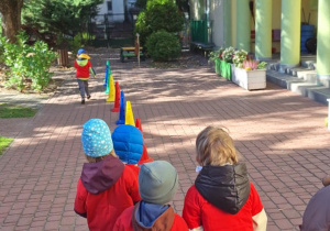 Dzieci kolejno przebiegają slalomem między pachołkami.