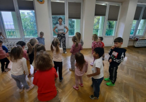 Przedszkolaki stoją w rozsypce na przeciwko prowadzącej.