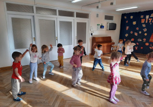 Dzieci tańczą do muzyki podnosząc rękę do góry i robiąc krok do boku.