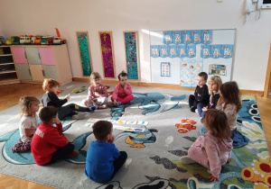 Maluchy siedzą w małym kole, na środku rozłożone są ilustracje z przyborami higienicznymi.