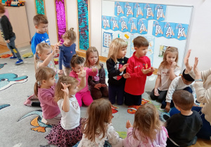 Nauczycielka wraz z dziećmi ogląda dłonie, do których przyczepiły się drobinki brokatu - symbolizujące bakterie.