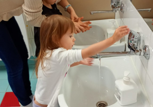 Nauczycielka pomaga chłopcu prawidłowo umyć dłonie.